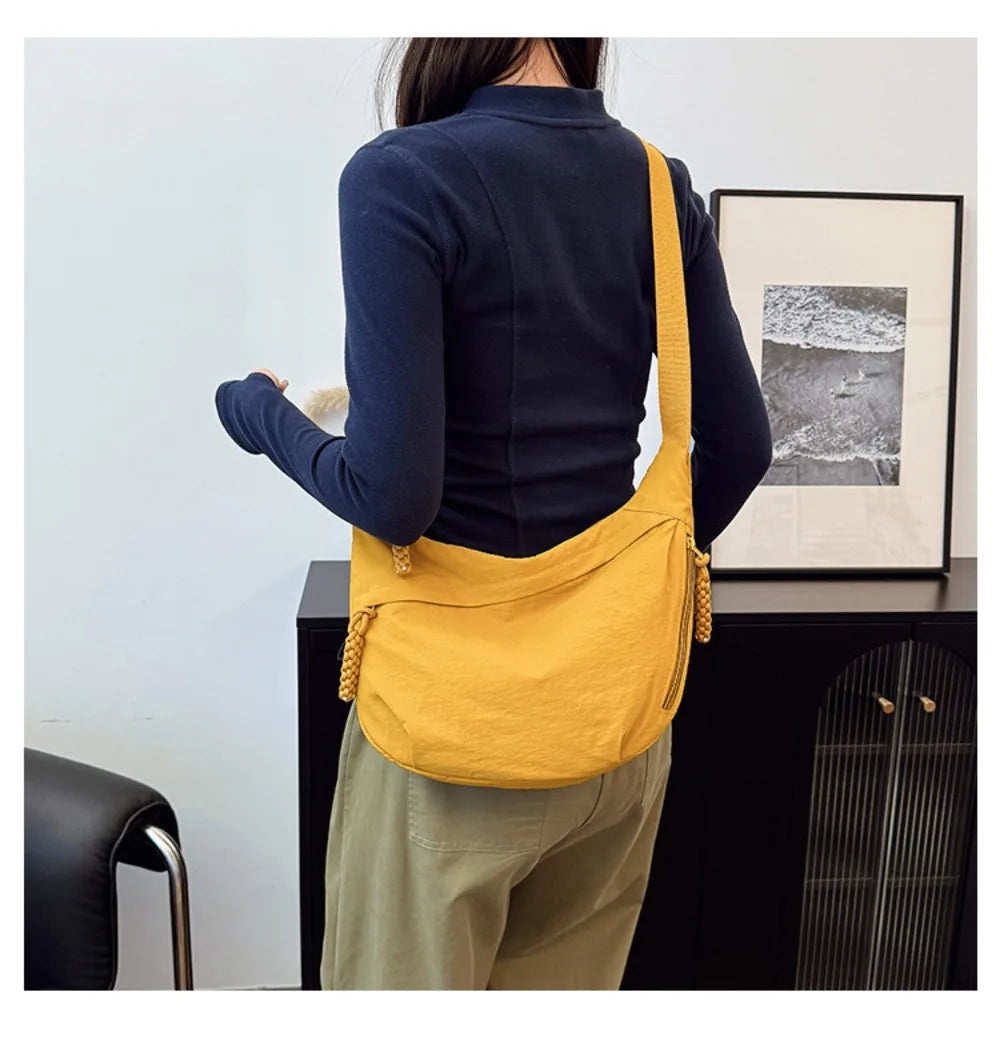 A woman wearing a navy blue sweater and olive pants holds a yellow canvas crossbody bag.