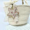 A beige woven bag features a starfish charm made of pink and clear rhinestones and lace.