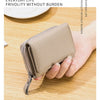 Cartera pequeña de cuero genuino de vaca color beige claro con cremallera, sostenida en la mano sobre una superficie de mader