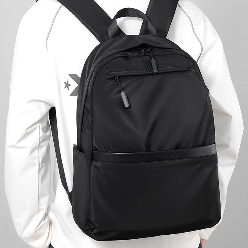 A black ultralight waterproof laptop backpack worn by a person in a white long-sleeved shirt.