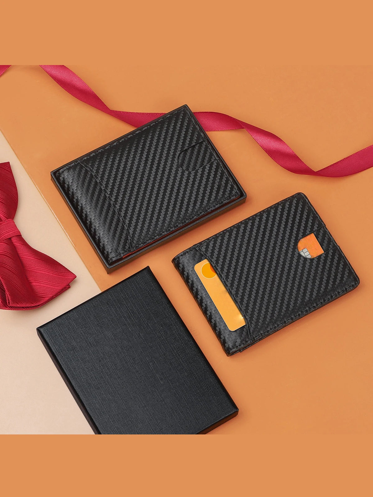 A set of black carbon fiber microfiber wallets and a red tie lying on an orange background.