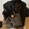 A person is holding a leopard print casual tote bag against a black jacket.