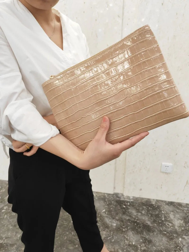 A woman holds a beige alligator print clutch bag against a light background.