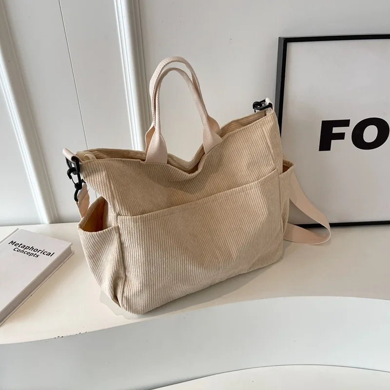 A beige corduroy multi-pocket tote bag with light tan straps is displayed on a white surface next to a framed sign.