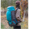 Une personne portant une casquette marron transporte un sac à dos d'escalade imperméable bleu sarcelle et gris dans une zone 