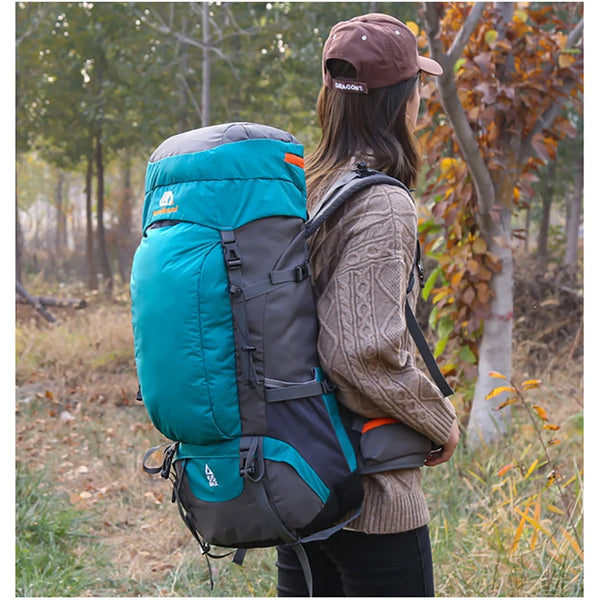 A person wearing a brown cap carries a teal and gray waterproof outdoor climbing backpack in a wooded area.