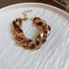 Gold-toned interlocking chain bracelet with amber and black leopard print beads on a white plate.