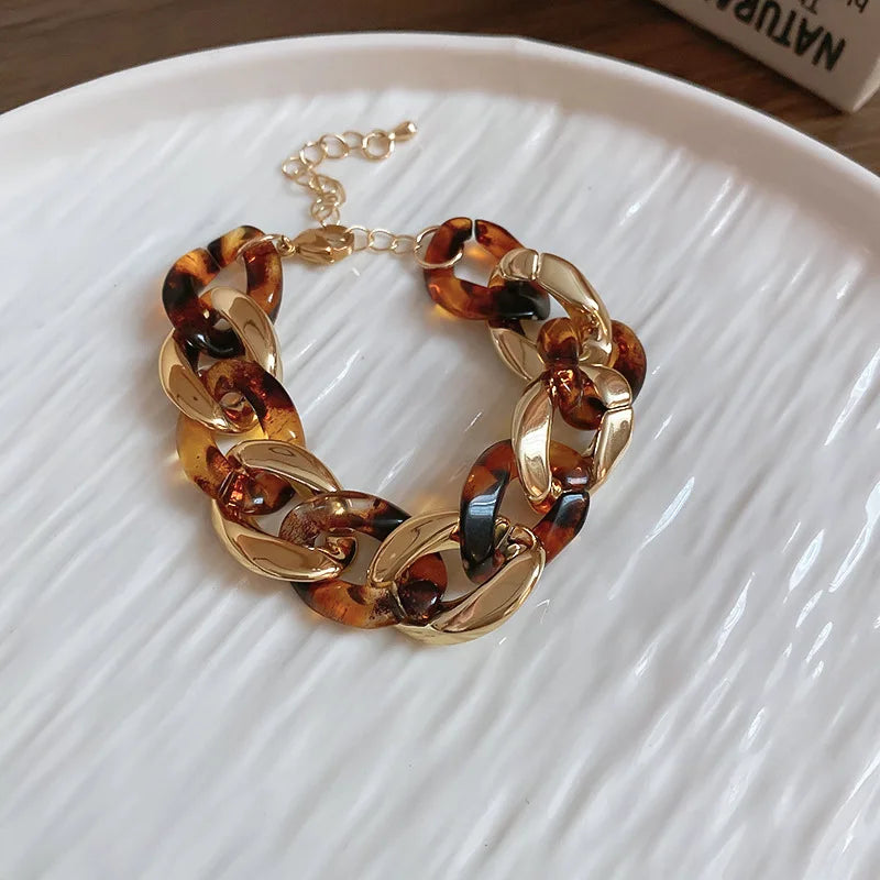 Gold-toned interlocking chain bracelet with amber and black leopard print beads on a white plate.