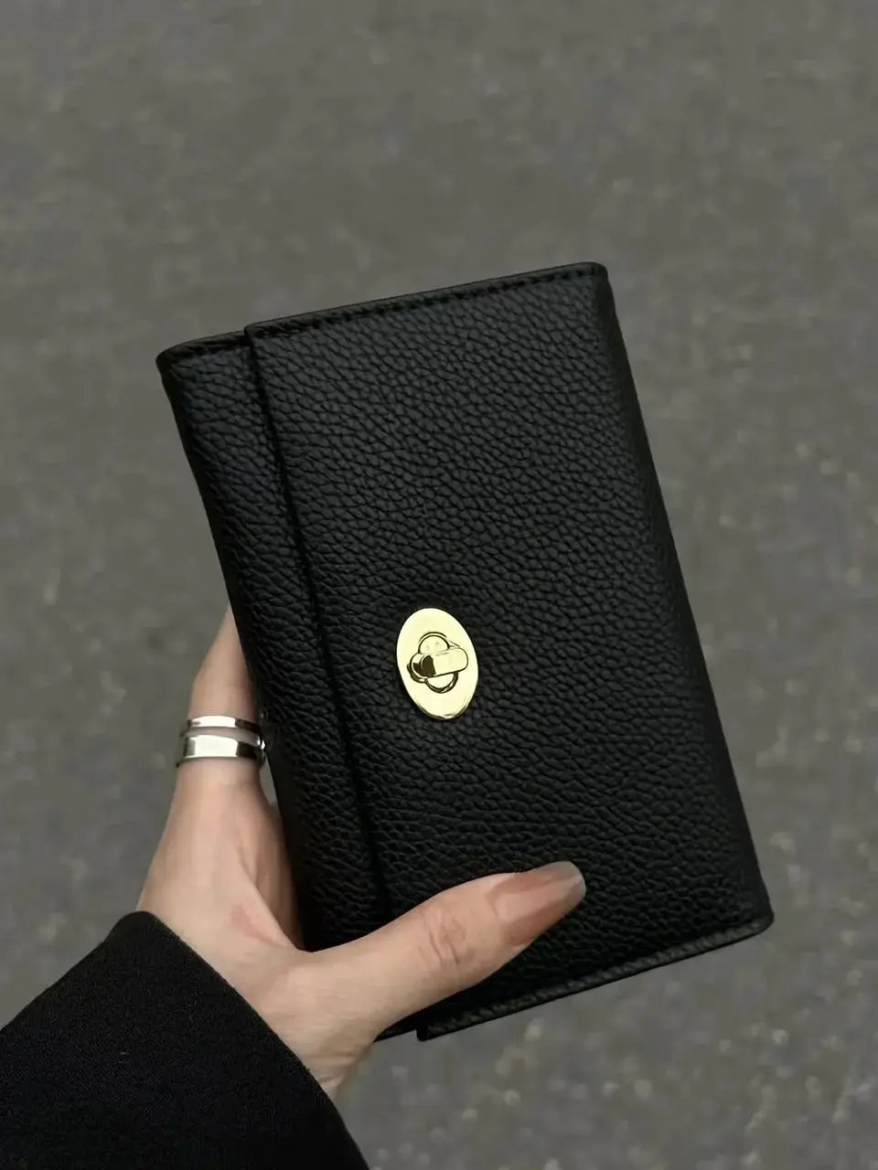 A hand holds a black card holder wallet with a gold embossed cloud design.