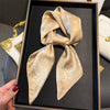 A silk hair scarf in beige and white paisley pattern is displayed in a black box.