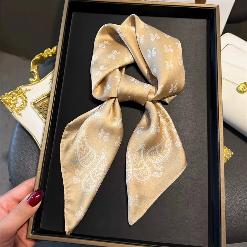 A silk hair scarf in beige and white paisley pattern is displayed in a black box.