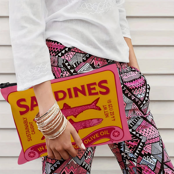 A hand holds a yellow makeup pouch labeled SADINES with a pink background against a white shirt and patterned pants.