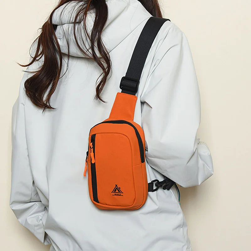 An orange nylon sling crossbody bag is worn on a white jacket.
