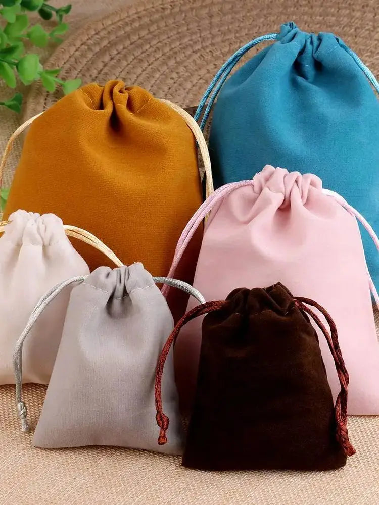 Colección de cinco bolsas de regalo de terciopelo suave con cordón en tonos naranja, azul, rosa, gris y marrón.