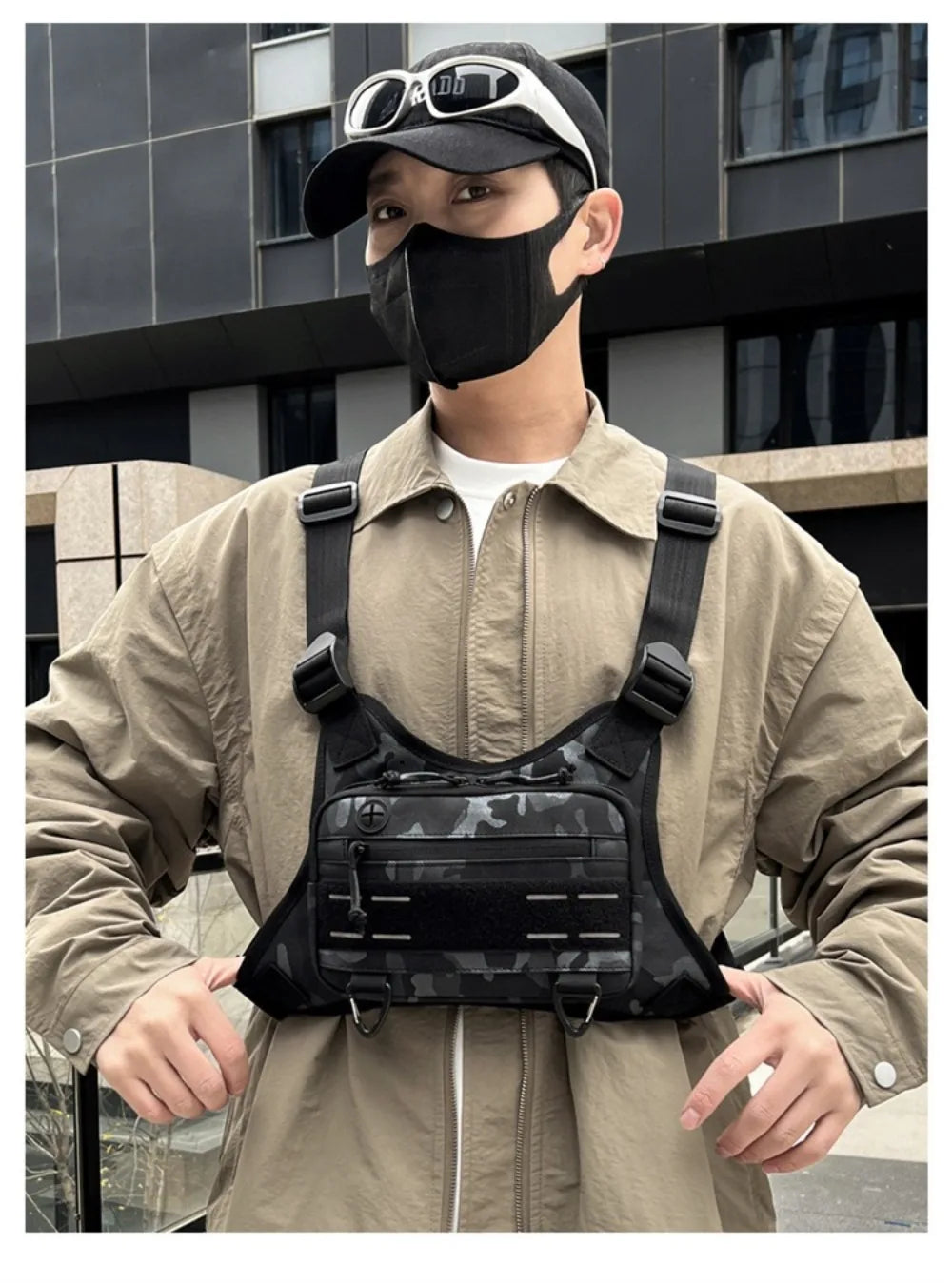 Un homme portant un masque noir et une veste beige tient un sac de sport noir multi-usage.