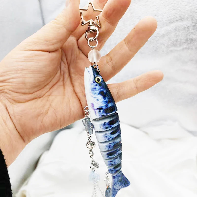 A hand holds a silver fish-themed acrylic keychain charm with a star top and a translucent fish pendant.