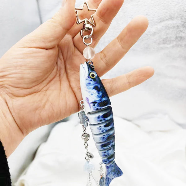 A hand holds a silver fish-themed acrylic keychain charm with a star top and a translucent fish pendant.