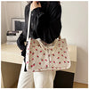 A woman holds a cream canvas tote bag featuring a red strawberry pattern against a light background.