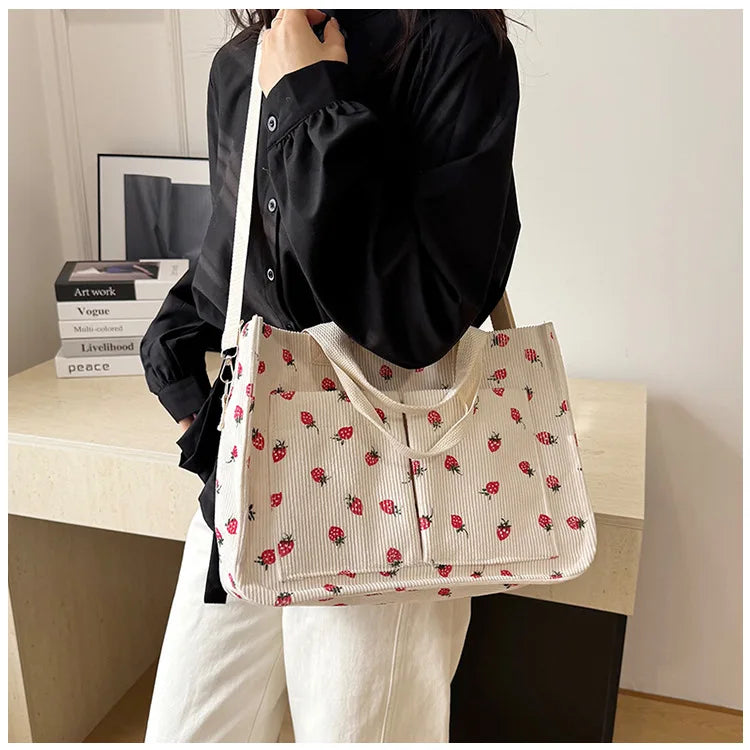A woman holds a cream canvas tote bag featuring a red strawberry pattern against a light background.
