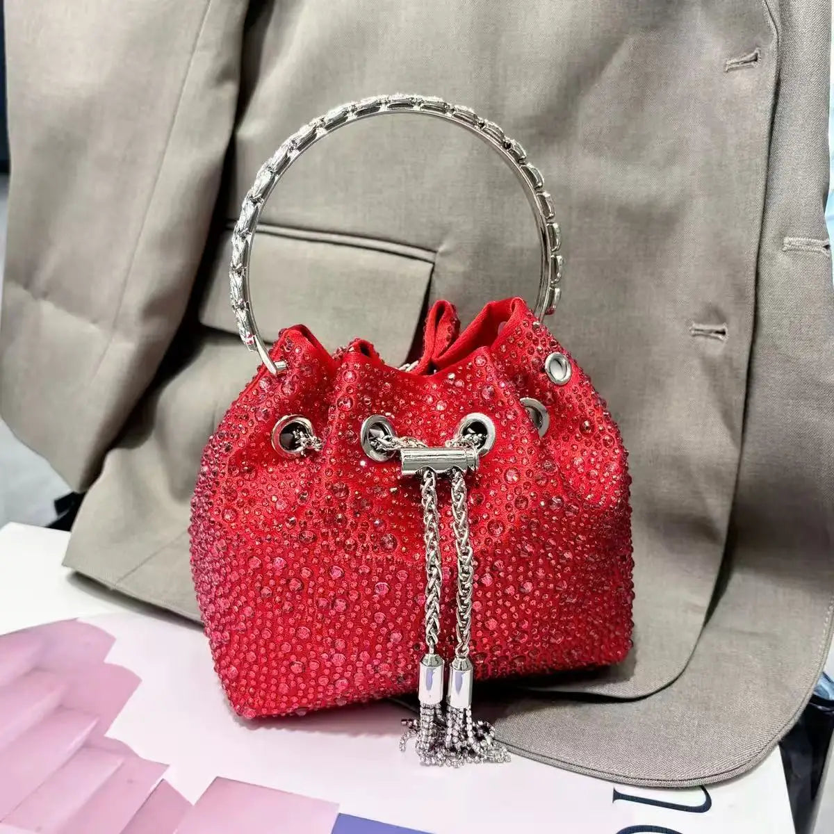 A red crystal-embellished evening clutch with a silver chain, resting on a light gray blazer.