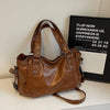 A brown leather shoulder bag is displayed on a white surface next to a framed sign.