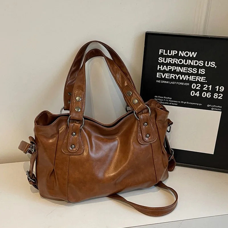 A brown leather shoulder bag is displayed on a white surface next to a framed sign.