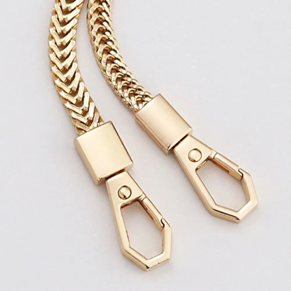 A close-up of a gold-colored metal chain strap for a handbag, featuring a woven texture and a clasp.