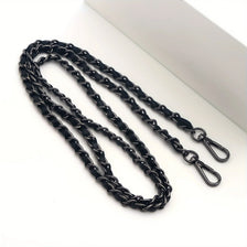 Black adjustable metal crossbody purse strap laid diagonally on a white surface.