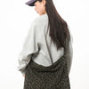 A woman wearing a purple cap and light gray sweater holds a black canvas camouflage shoulder bag.