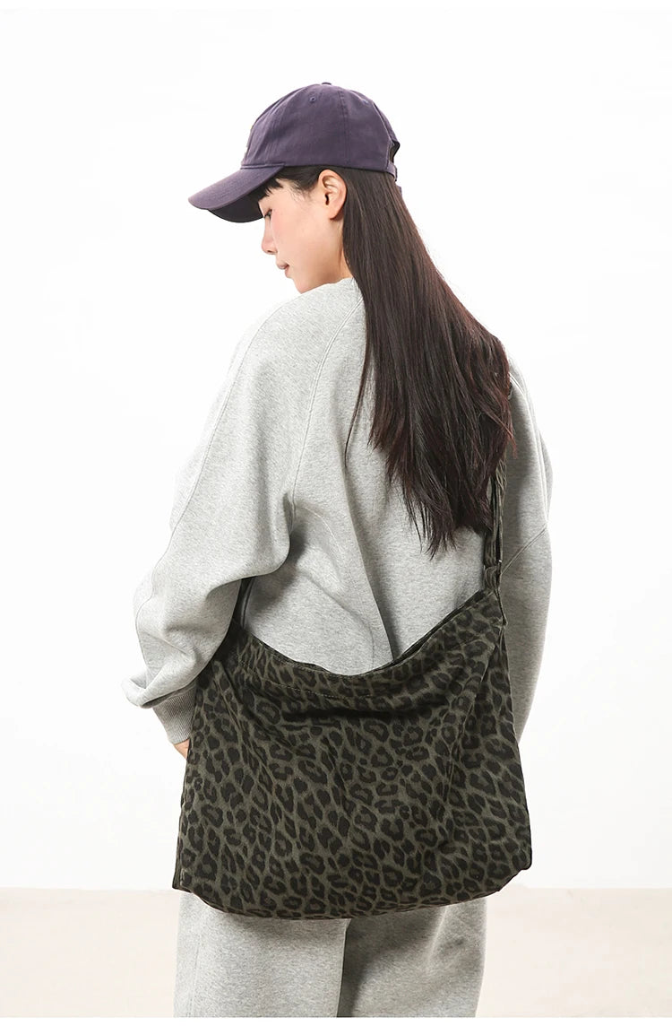 A woman wearing a purple cap and light gray sweater holds a black canvas camouflage shoulder bag.