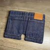 A dark indigo denim wallet and card holder with a tan leather flap resting on a wooden surface.