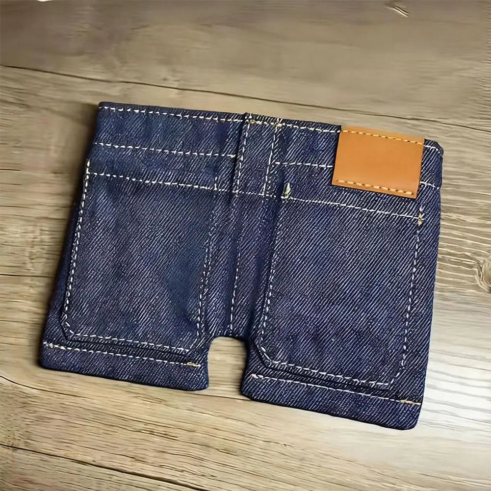 A dark indigo denim wallet and card holder with a tan leather flap resting on a wooden surface.