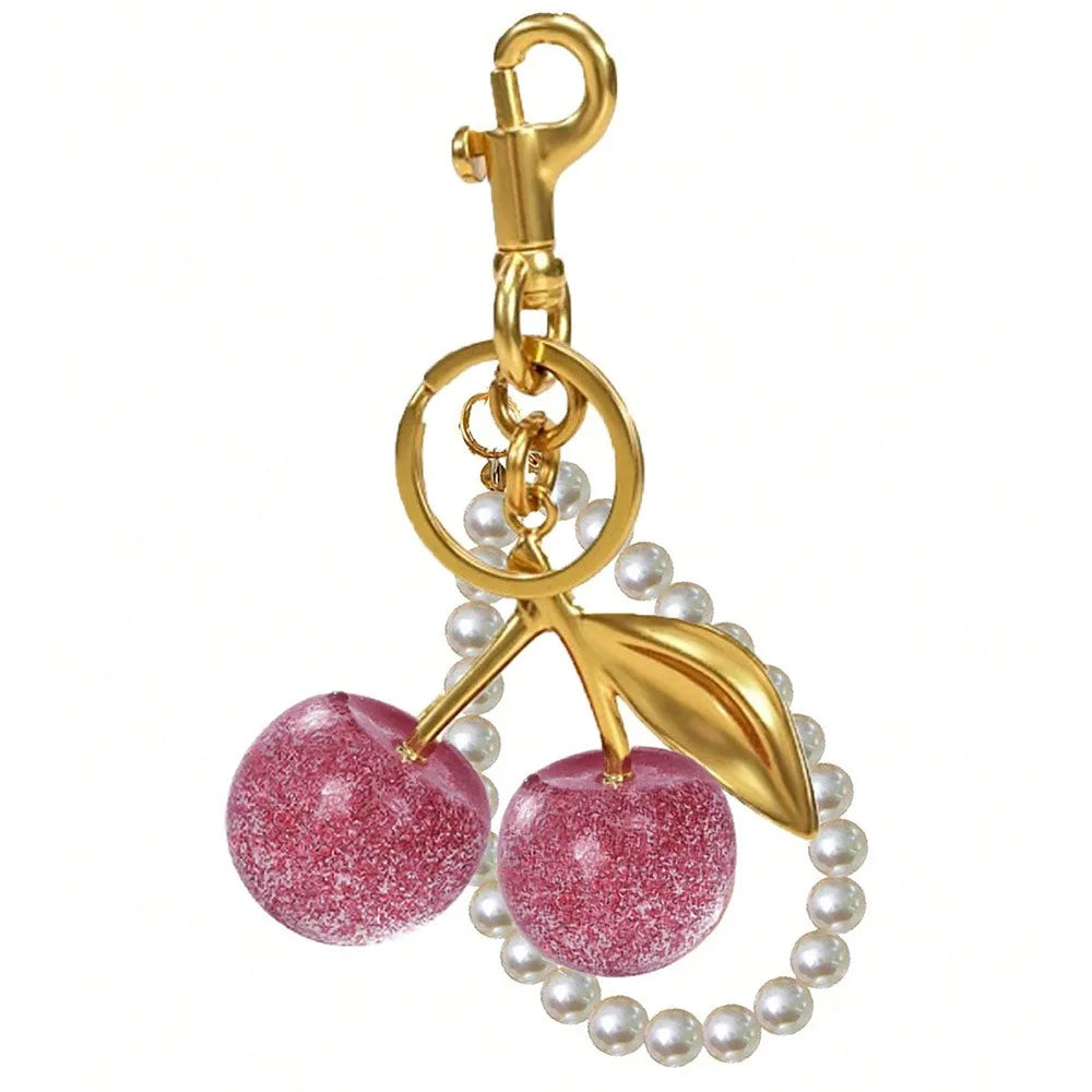 ميدالية مفاتيح بلون ذهبي مزينة بقلادة كرز وردية لامعة وحبات لؤلؤ.