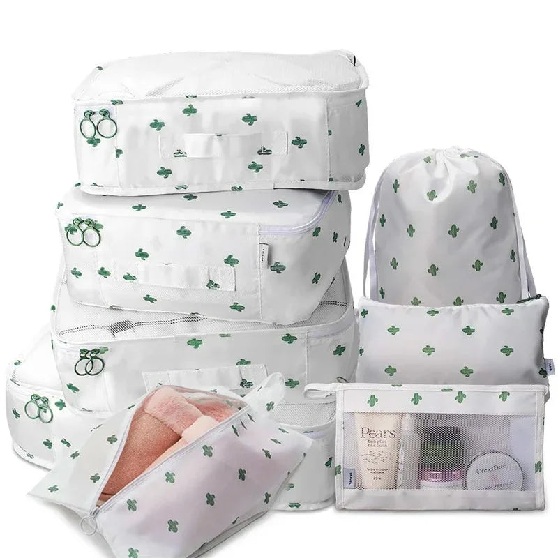 A set of white mesh packing cubes in various sizes with green leaf patterns for travel organization.