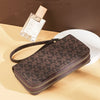 A dark brown patterned PU leather zippered wallet is displayed next to a glass perfume bottle on a light beige surface.