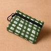 A green and white plaid mini coin purse with a black zipper and carabiner clip resting on a beige surface.