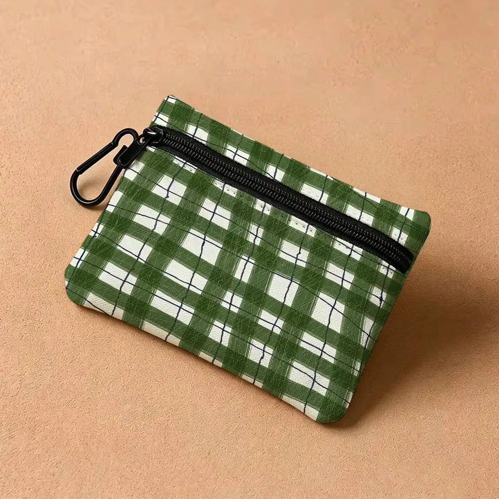 A green and white plaid mini coin purse with a black zipper and carabiner clip resting on a beige surface.