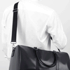 Maleta duffel de cuero negro con correa negra puesta sobre una camisa blanca.