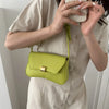 A woman holds a lime green leather crossbody bag against a light beige shirt.