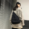 A woman wearing a light beige sweatshirt holds a black canvas crossbody shoulder bag in a modern indoor setting.