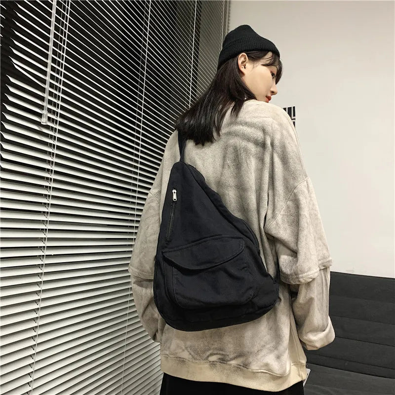 A woman wearing a light beige sweatshirt holds a black canvas crossbody shoulder bag in a modern indoor setting.