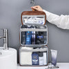 A brown cosmetic organizer bag with clear compartments and a white dispenser is being held by a hand.
