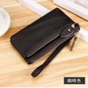 A black genuine leather wristlet clutch wallet with a gold zipper closure resting on a wooden surface.