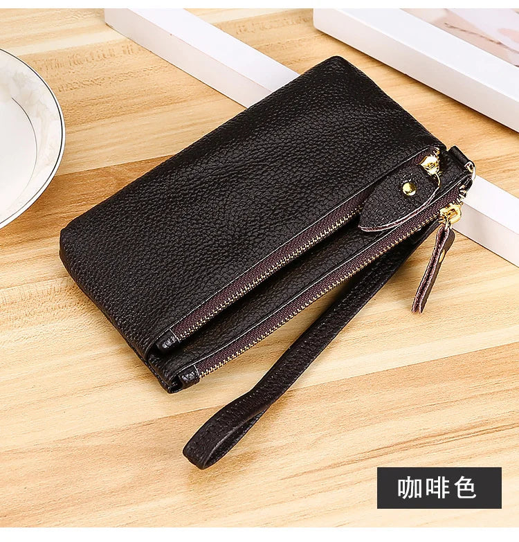 A black genuine leather wristlet clutch wallet with a gold zipper closure resting on a wooden surface.