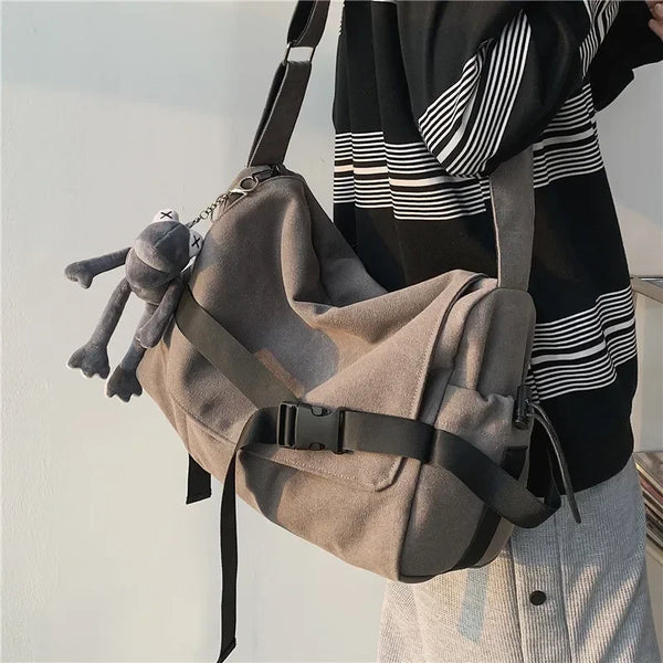 A canvas crossbody bag in beige leather is being worn by a person, with a dark sweater visible.