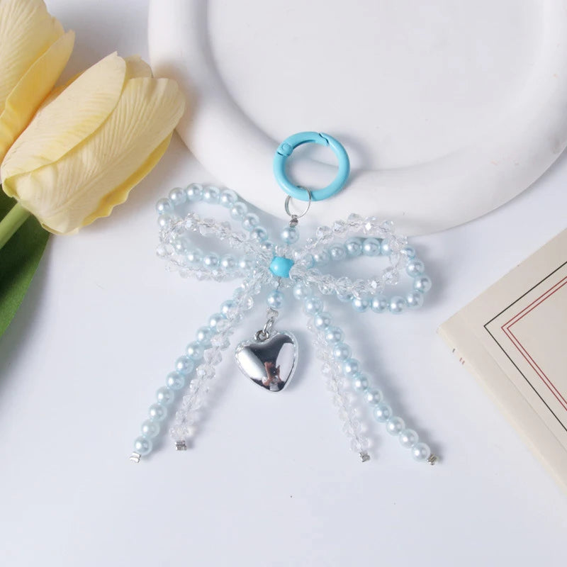 A light blue pearl keychain featuring a bow knot design and a heart charm, placed next to a yellow tulip.