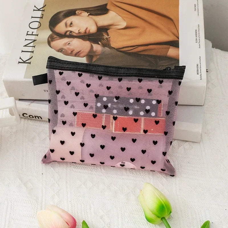 A pink mesh cosmetic storage pouch with a heart pattern and rectangular accents rests on a white surface.