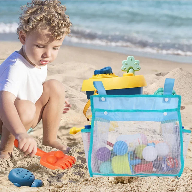 A young child is playing with a hanging bath toy organizer bag filled with colorful toys on a sandy beach.