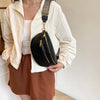 A woman wearing a cream jacket and brown skirt holds a black PU leather crossbody bag with a patterned strap.