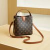 A brown leather bucket bag with a gold-toned strap and patterned fabric resting on a light wooden surface.